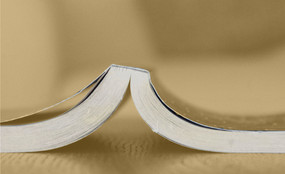 A book lies open and face-down on a desk.