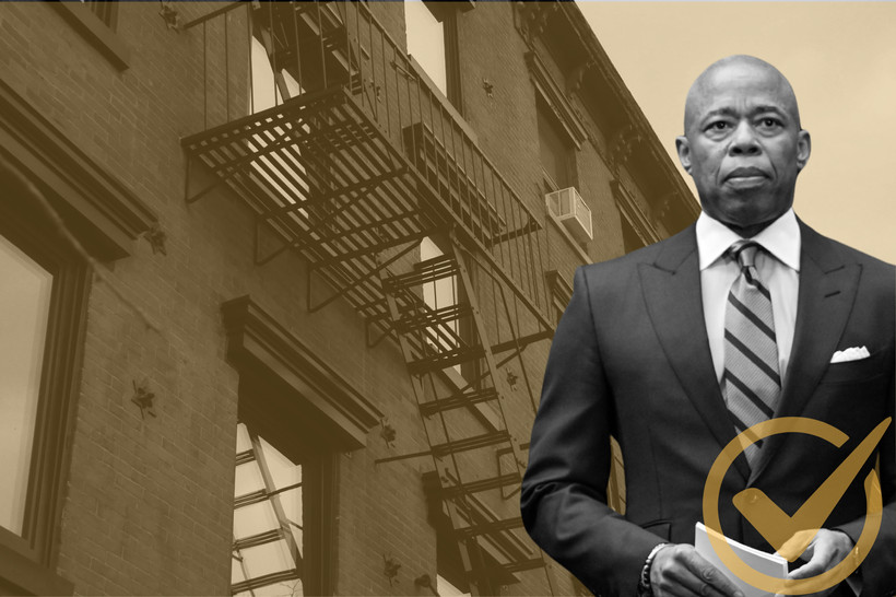 Mayor Eric Adams standing in front of an apartment building.