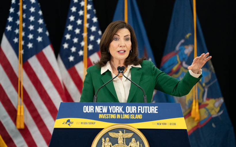 New York State Governor Kathy Hochul stands in front of American flags and behind a podium reading "Our New York, Our Future."