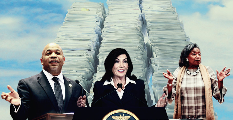 Assembly Speaker Carl Heastie, Governor Kathy Hochul, and Senate Majority Leader Andrea Stewart-Cousins before three tall stacks of paper.