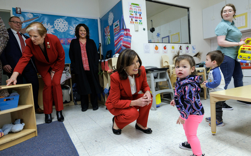 New York governor Kathy Hochul kneels in a red suit with a child looking out in distress