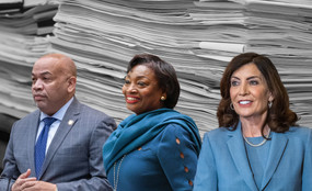 Carl Heastie, Andrea Stewart-Cousins, and Kathy Hochul stand in front of a large pile of papers.
