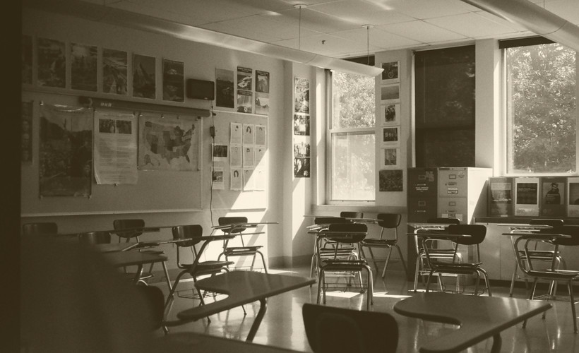 An image of a classroom with two windows and many empty desks.