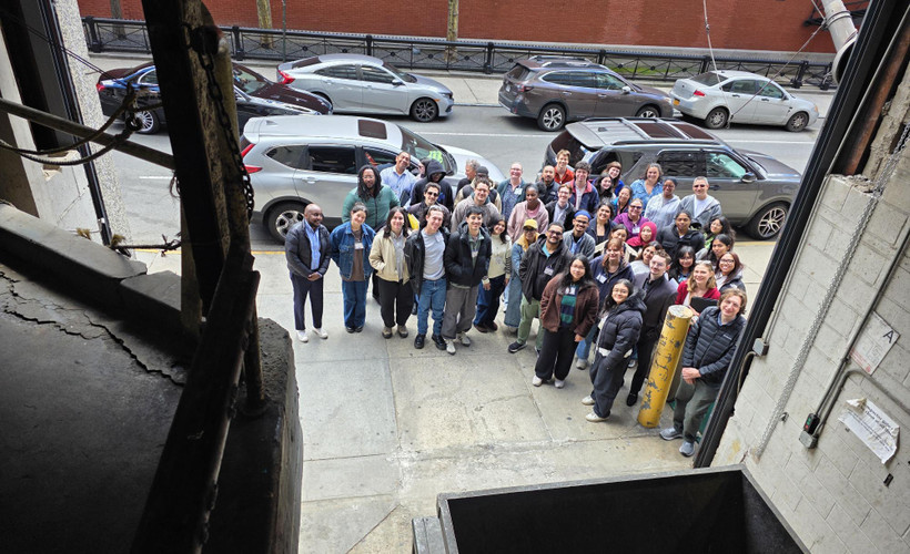A group of about 50 people pose for a photo taken from inside a garage housing a trash compactor.