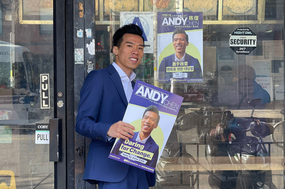 Assembly candidate Yi Andy Chen, in a blue suit, puts up his own campaign posters on a glass door that says PULL.