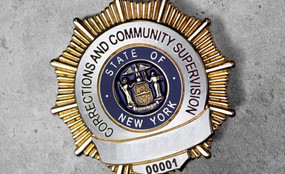 A close-up photo of a New York State DOCCS badge on a concrete background.