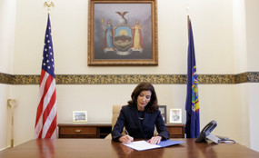 New York Governor Kathy Hochul sits at a large wooden table and signs papers in Albany, New York.
