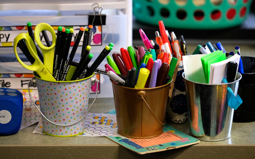 Three small pails sit atop a counter, one filled with pencils, another filled with markers, and another filled with sticky notes.