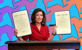 Governor Kathy Hochul holds two signed bills, superimposed over a background showing the state of New York.