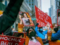 In a protest crowd, a closeup on one protester holding a sign that says "Hochul: Build of Burn"