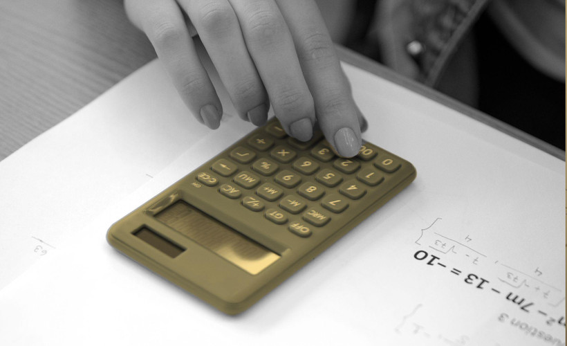 A student's hand using a calculator on a math worksheet.
