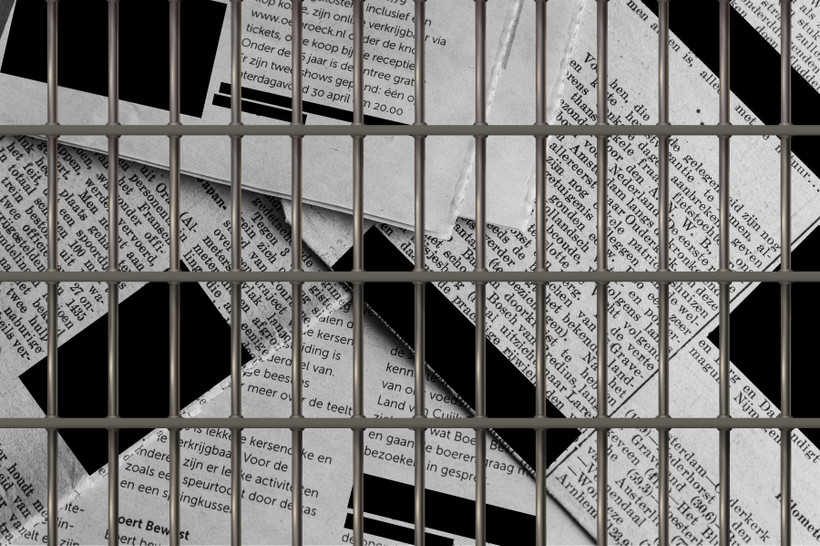 a stack of newspapers, with redaction boxes covering the text, behind prison bars