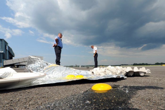 A yolk on asphalt next to a piece of aluminum foil. Two men looking down