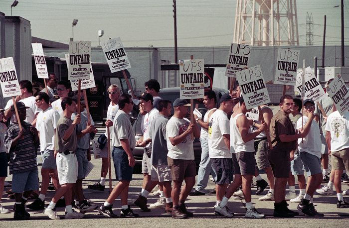 A group of men stand in a picket line, holding sings that read, "UPS unfair to Teamsters Local Union 396."