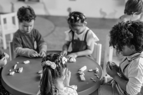 Four young children sit around a table, playing with clay.