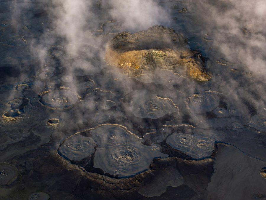 Mist rises over a barren landscape with a single green patch