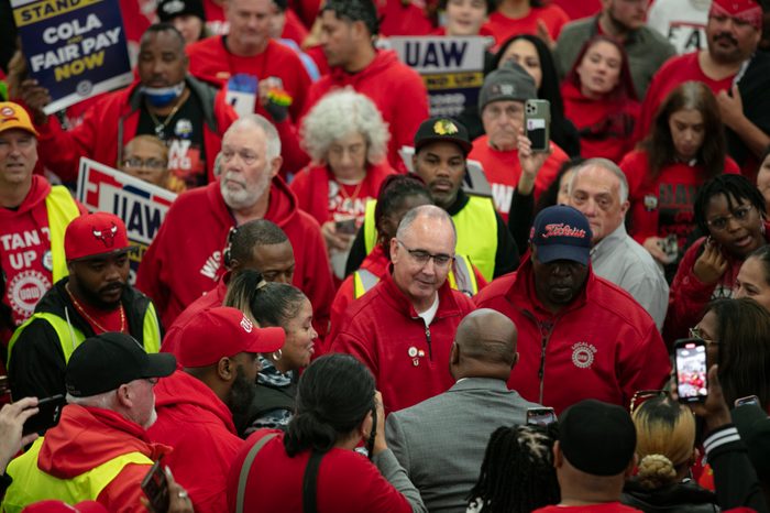 A crowd gathers, most of them wearing red shirts and some of them holding signs that read UAW.