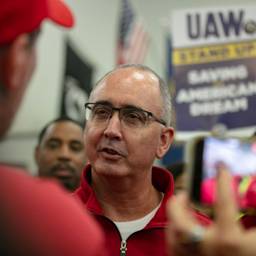 Closeup of Shawn Fain mid-speaking to a worker who is facing away from the camera; UAW strike sign in the background.