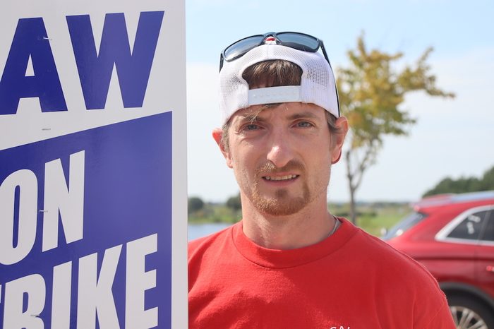 Closeup of a worker with a backwards baseball cap holding a sign that partially reads "UAW on strike"