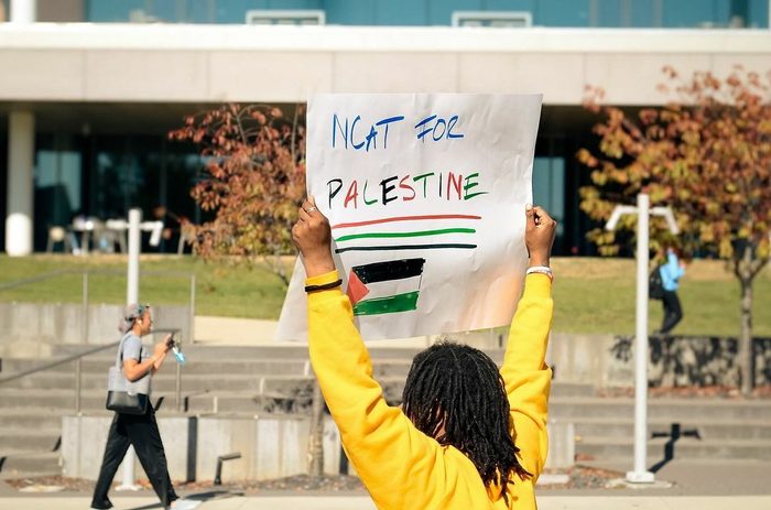 Student holds up "NCAT for Palestine" sign in red, green and black lettering while students walk by