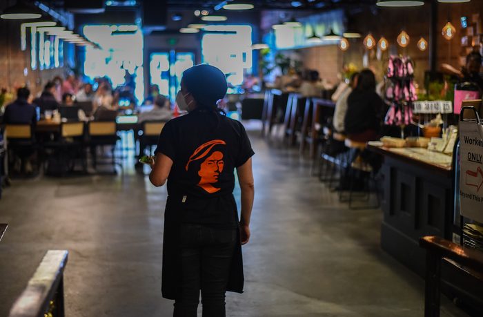 Back shot of a worker with a radical t shirt entering a large open cafe with overhead lights