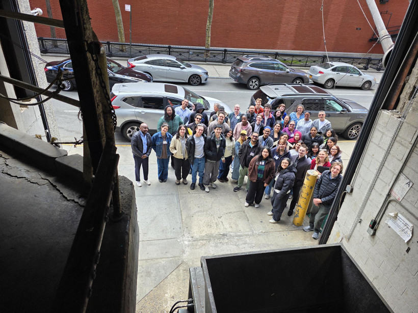 A group of about 50 people pose for a photo taken from inside a garage housing a trash compactor.