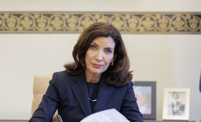 Kathy Hochul stares into the camera while signing papers