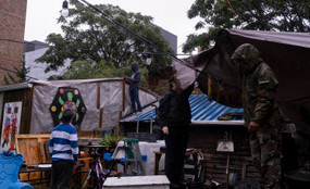 Various figures hang up tarps in the rain at Bushwick City Farm.