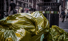 Bags of trash with a golden filter sit in front of a trash can on the curb in New York City