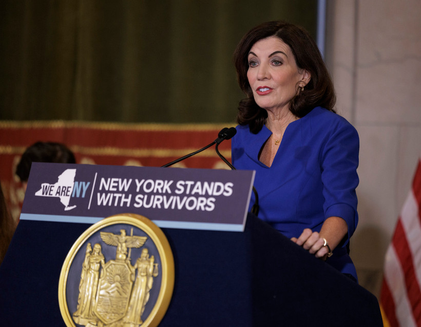Kathy Hochul stands at a podium that bears a sign reading "New York stands with survivors."