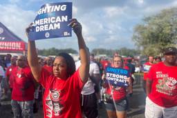 Photograph of a worker in a red shirt holding a sign that says "Fighting for the American Dream," with other marching behind her.