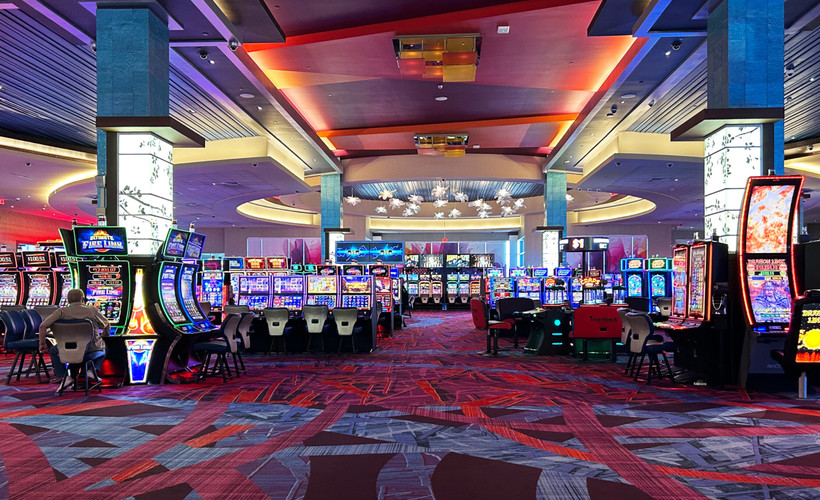 Photo of a casino floor with rows of brightly lit video lottery terminals and a single player sitting to the left in front of a terminal.