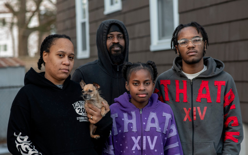 The Stradford-Moses family stands outside its home. Jasmine Stradford holds one of the family’s dogs in her hand.
