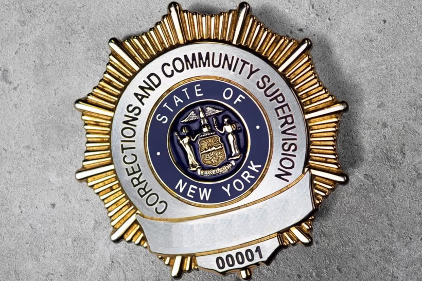 A close-up photo of a New York State DOCCS badge on a concrete background.