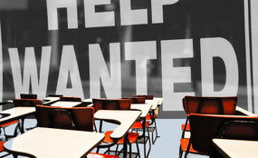 Empty schoolroom chairs face a large help wanted sign.