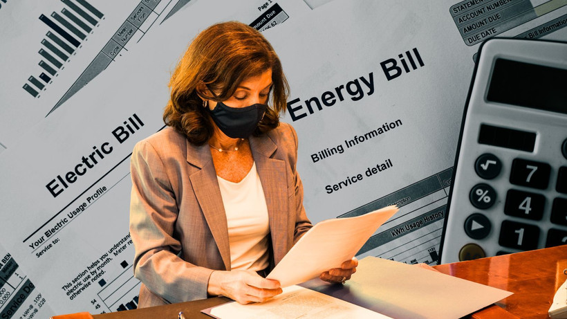 Hochul reading a piece of paper against the backdrop of energy bills