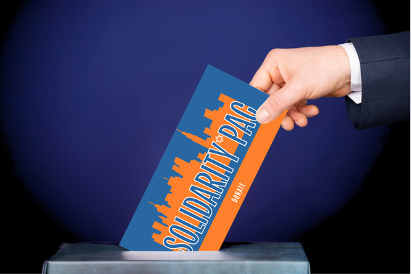 A hand places a ballot with the Solidarity PAC logo in a ballot box.