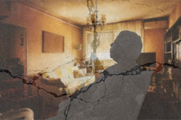 A silhouette of an elderly person sitting alone in a chair in a warm living room. Cracks appear over the image, indicating precarity.