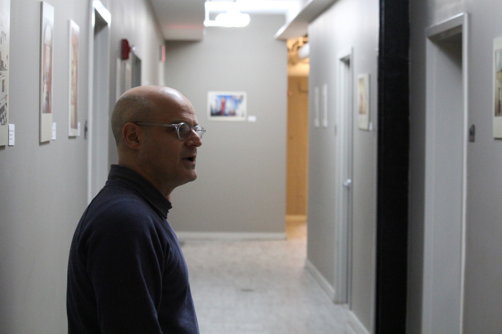 A bald man in glasses stands in a hallway.