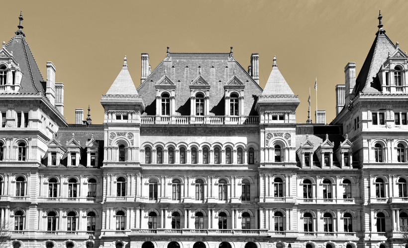 A black and white photo of the New York state Capitol Buildling over a yellow-tinted background.