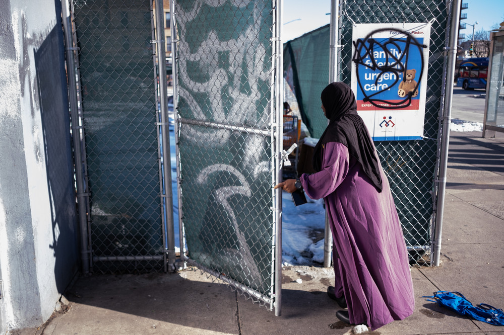 A woman in a purple dress and a black head covering opens a gate.