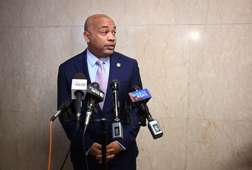 New York State Assembly speaker Carl Heastie stands in front of a tile wall with TV microphones.